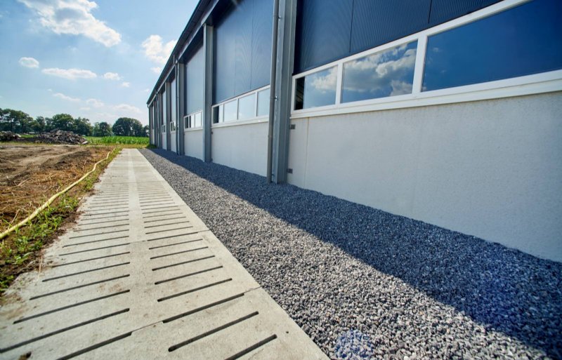 Buiten tegen de stal aan ligt over twee meter breedte een strook met scherpe stenen. Dat is een van de maatregelen die ervoor gaat zorgen dat ongedierte de stal niet binnen kan komen. Via het rooster gaat de verse lucht onder de stal door naar de andere kant.