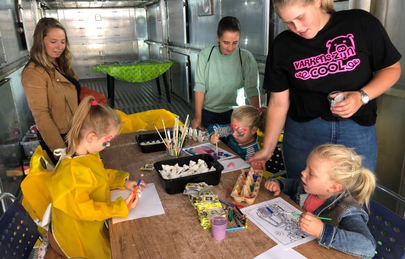 In de laadruimte van de vrachtwagen op het erf bij familie Van Son in Valkenswaard zijn kinderen creatief bezig met varkens.